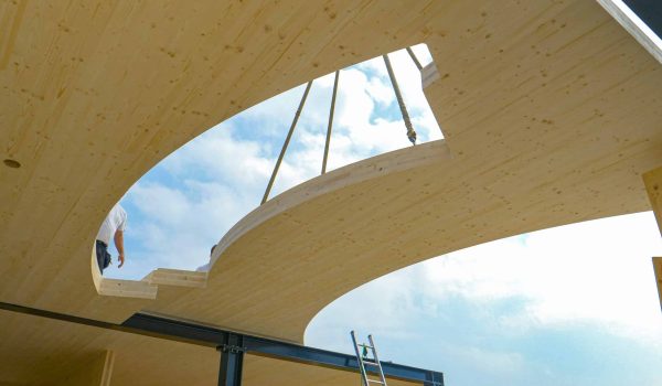 CLOSE UP: Contemporary CLT house is being assembled on a sunny spring day. Opening in the wooden ground of the top floor of a glued-laminated timber house offers a view of workers and clear blue skies